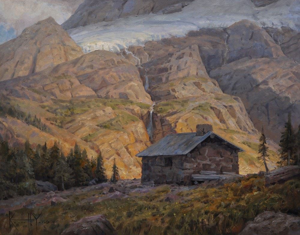 A small stone building stands in a green and yellow meadow surrounded by mountains and small waterfalls.