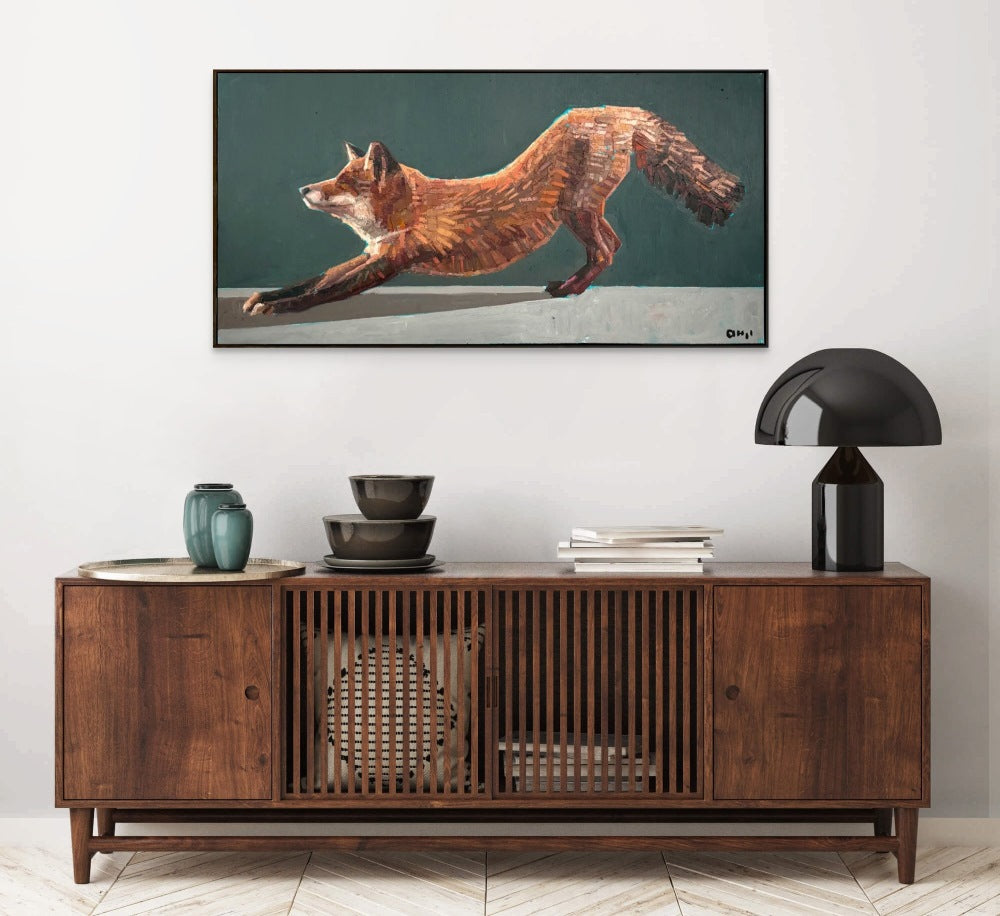 A mid century modern style wooden cabinet sits below a painting of a fox stretching.