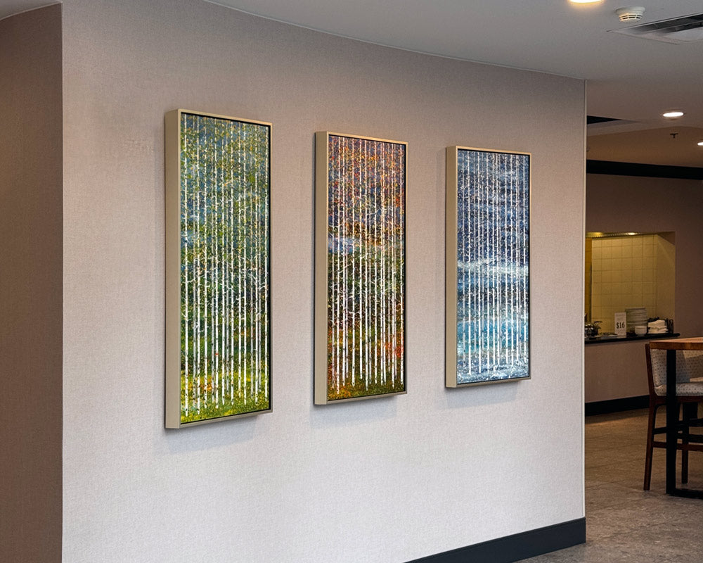 Three colorful contemporary drip paintings of aspens are hung on a beige wall in the Hilton Garden Inn in Kalispell.