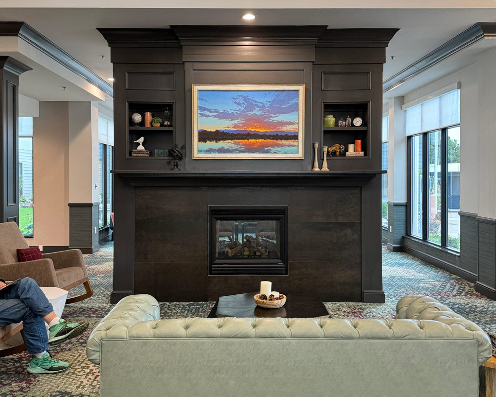 A view of the sitting room of a hotel lobby fireplace with a Johne Richardson oil painting on the mantel depicting a sunset above a lake.