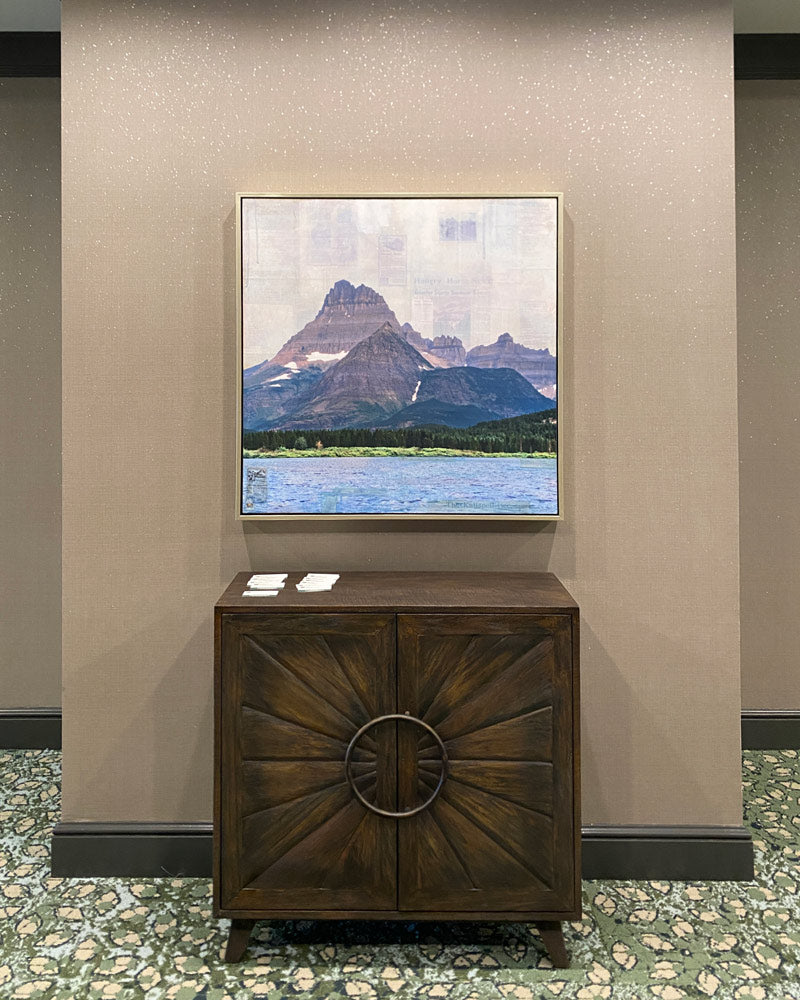 A square mixed media piece depicting Heavy Shield, also known as Mount Wilson, hung above a dark brown end table.