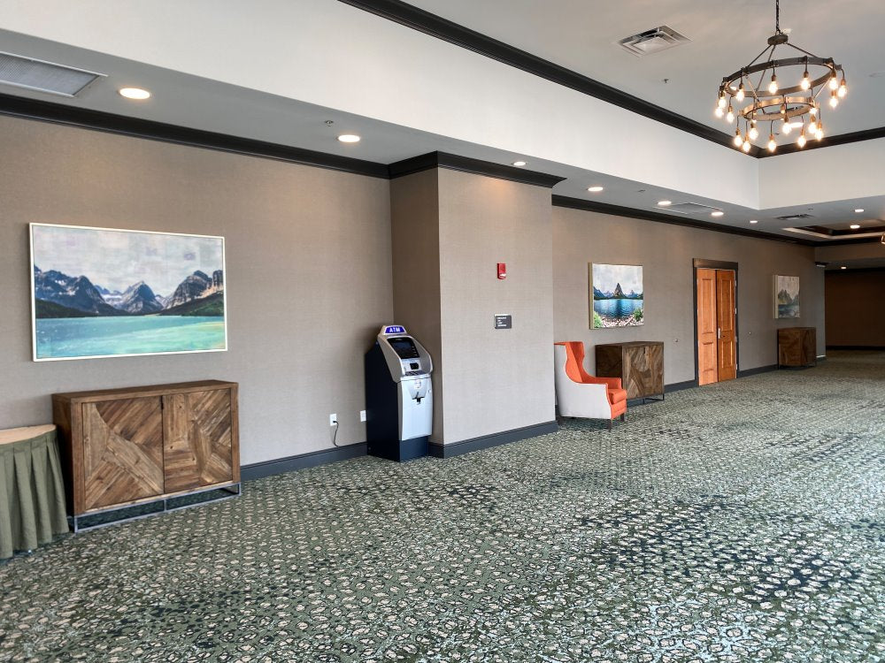 A view of a hotel lobby with bright natural light, contemporary barn wood cabinets, an Edison bulb chandelier, and two large pieces of artwork depicting lake scenes in Glacier National Park.