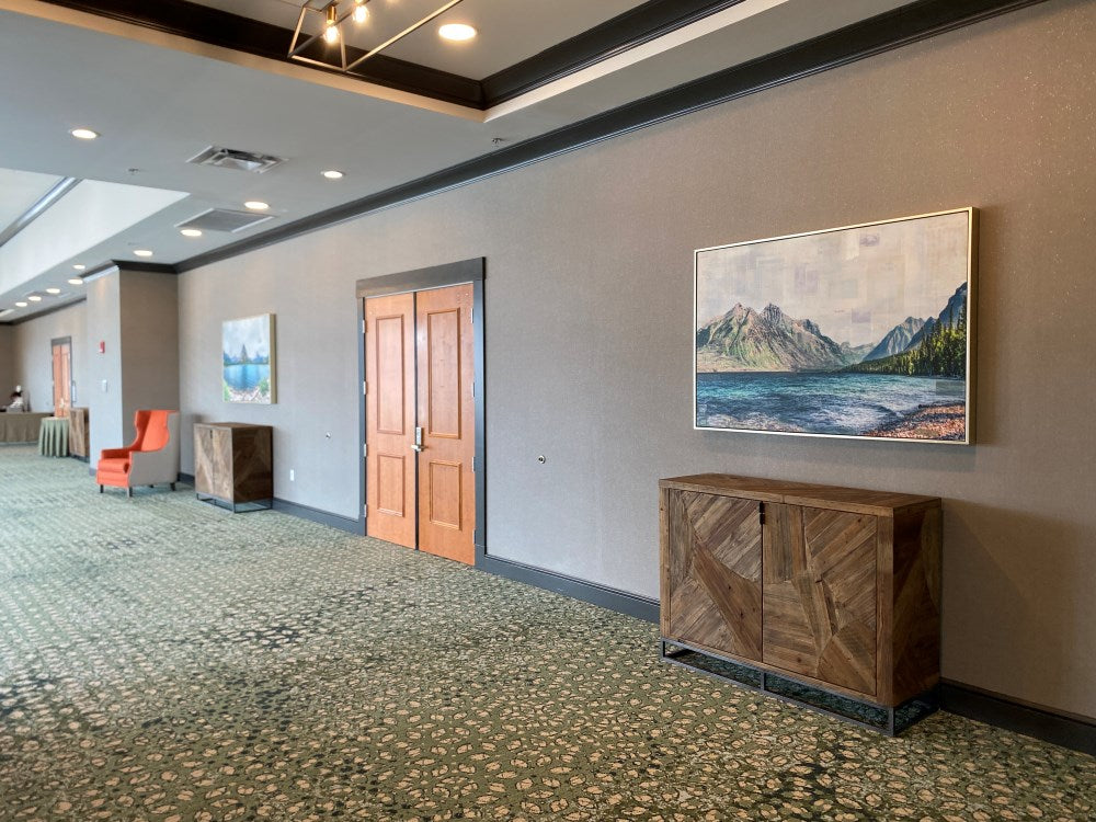 A photo of a hotel lobby with bright natural light, contemporary furnishings, and a mixed media piece by JC Spock featuring the view from Lake McDonald in Glacier National Park.